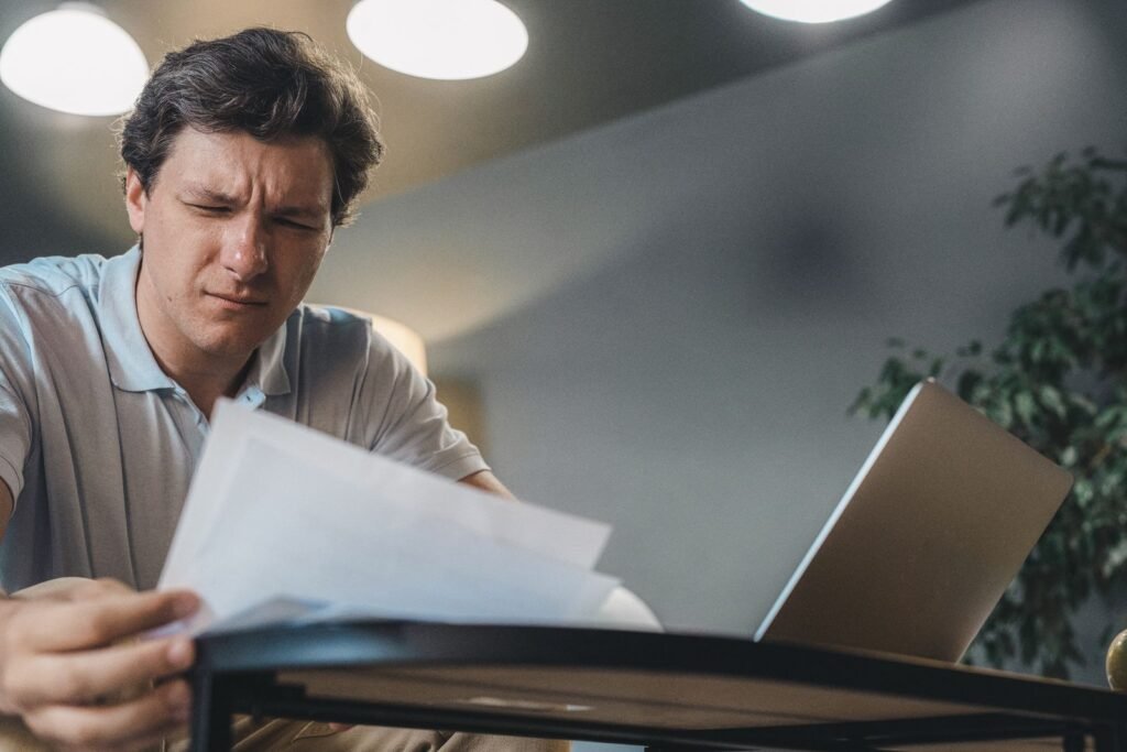 شخص يراجع مستندات على مكتب أمام حاسوب محمول؛ صورة فوتوغرافية تعبيرية